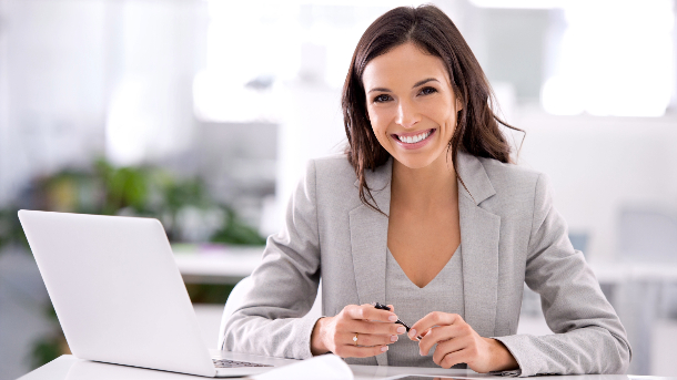 Female smiling wearing a suite, with a laptop open on a desk